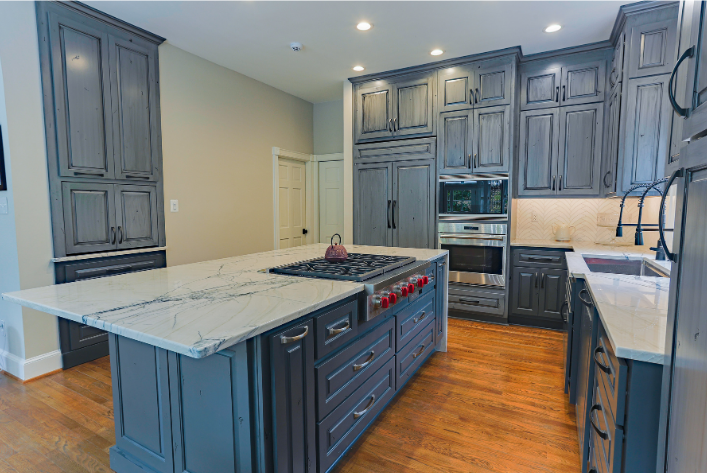Renovated kitchen with blue-gray custom cabinetry, marble island, and gas cooktop